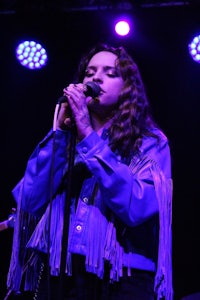 a woman in a purple jacket singing into a microphone